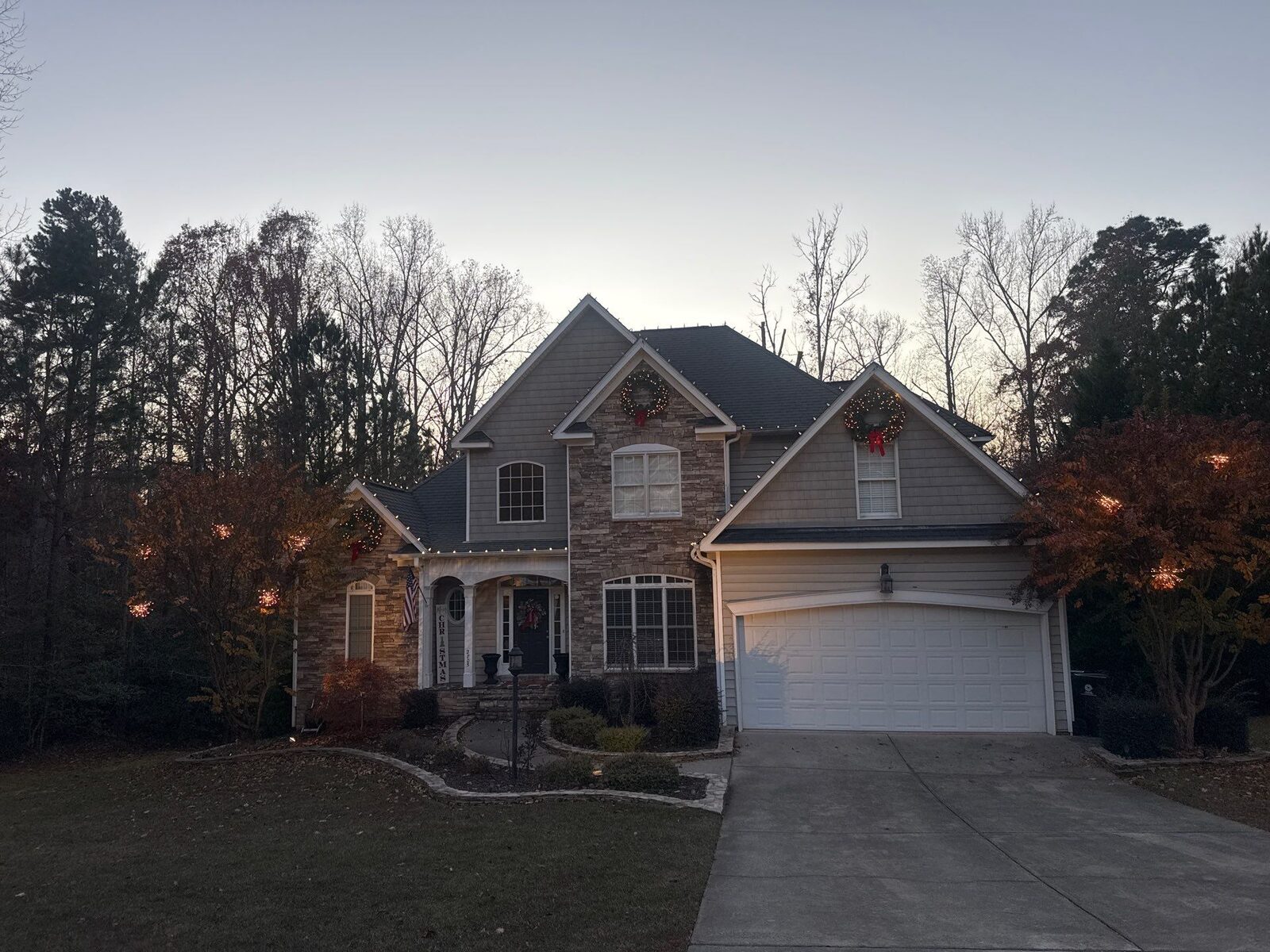 Stone craftsman home with Christmas roofline lights and lit wreaths